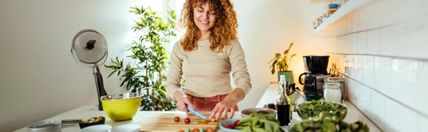 A woman is cutting vegetables in a kitchen filled with plants