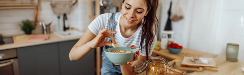 A woman is eating muesli from a bowl in the kitchen