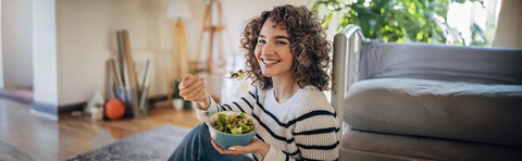 A woman is sitting on the floor and eating from a bowl