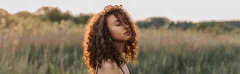 A woman with curly hair is standing in a grain field