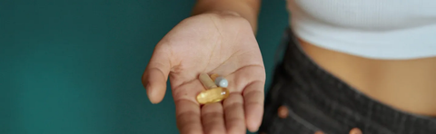 An open palm holding two capsules in front of a person’s abdomen, who is wearing athletic clothing