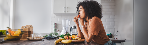 A woman is eating in the kitchen; fruit is on the countertop