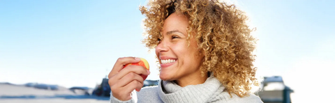 A woman with blonde curls is eating an apple outdoors