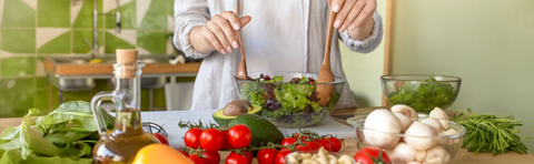 Person bereitet Salat zu, auf dem Tisch Gemüse, Öl und Pilze