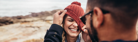 A couple is laughing together; the woman is pulling her hat down over her face