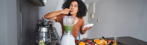 A woman is tasting a green smoothie in the kitchen