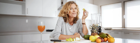 Frau steht in der Küche an einer Theke mit Obst und einem Mixer