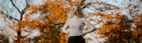A woman stands in front of trees with autumnal colors