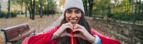 A woman wearing a hat forms a heart with her hands in the park