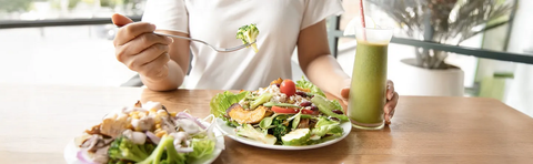 Person isst einen Salat, daneben ein grüner Smoothie