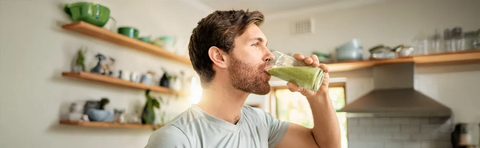 A man is drinking a green smoothie in the kitchen