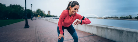 A woman in athletic clothing is looking at her watch on a promenade