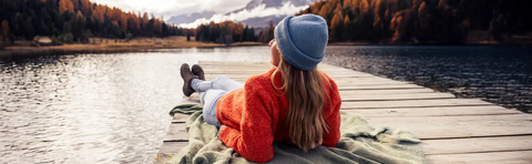 Frau in rotem Pullover liegt auf einem Steg am See, Blick auf die Berge