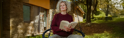 A woman is reading a book in a hanging chair in the garden