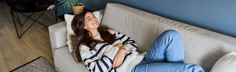 A woman is lying relaxed on a sofa and smiling