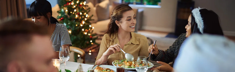 Menschen essen gemeinsam an einem festlich gedeckten Tisch mit Weihnachtsbaum