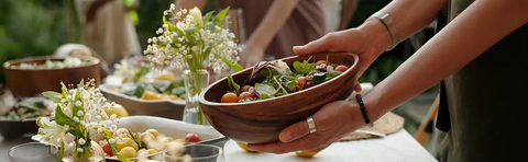 A hand is passing a bowl of salad across a festively set table