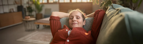 A woman is lying relaxed on a sofa with her eyes closed