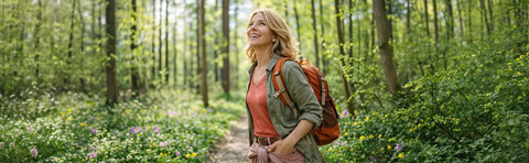 A woman with a backpack is hiking through a sunny spring forest