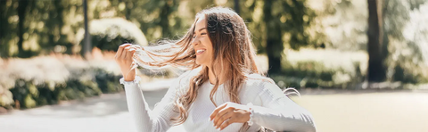 A woman runs her fingers through her hair, laughing, backlit