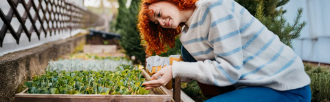 A woman with red hair is working in a raised garden bed