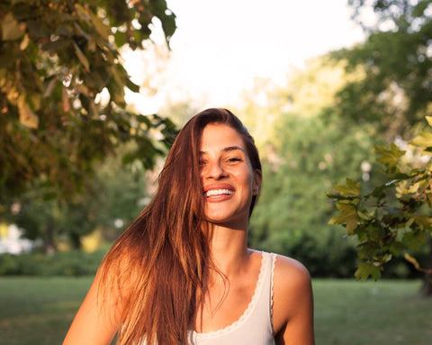 A smiling woman with long hair in a sunny park