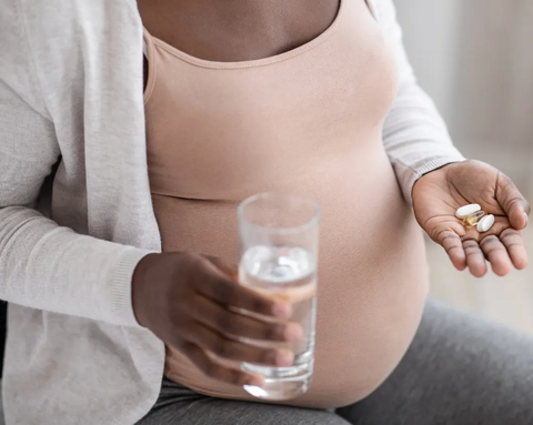 A pregnant woman is holding a glass of water and two capsules in her hands