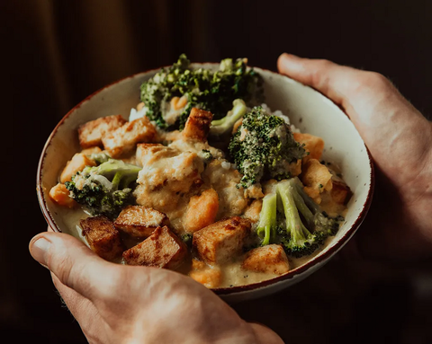 Hands are holding a bowl of tofu, broccoli, and vegetables