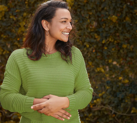 A smiling woman in a green sweater, with her hands in front of her stomach