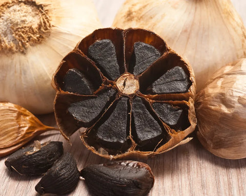 Nahaufnahme von schwarzem Knoblauch – gereifte Knoblauchknollen mit dunklen, weichen Zehen, umgeben von der hellbraunen Schale.
