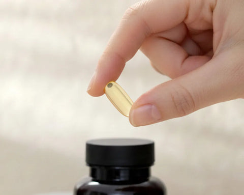 Eine Hand hält eine goldene, transparente Fischöl-Kapsel über eine Dose TISSO Pro Omega 3, die vor einem hellen, minimalistischen Hintergrund steht; Bildhinweis: KI-gestützter Inhalt