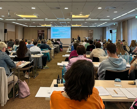 A fully occupied seminar room during a training session at the TISSO Academy; a view from the back, looking over the participants toward the presenter in front of the screen